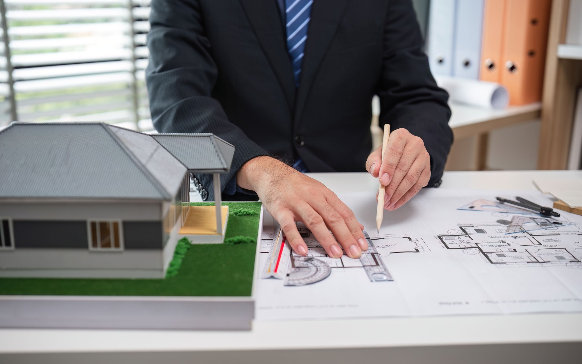 Real Estate Project Sales Representative Discussing Architectural Plans with Model House on Desk